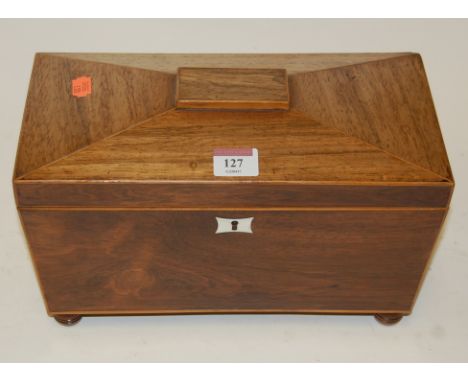 A Regency faded rosewood tea caddy of sarcophagus form having fitted interior flanked by lion mask ring handles on bun feet, 