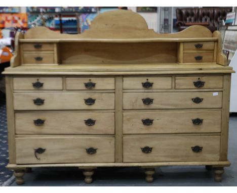 A Victorian pine oversized chiffonier of ten drawers, raised upstand with four short drawers and overall raised on six turned