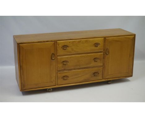 An Ercol light elm sideboard, having three drawers flanked by two panelled cupboard doors, raised on castors