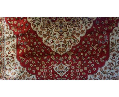 A Kum carpet, on a mainly red ground, the central panel with large red shaped medallion, with floral decoration, the whole su
