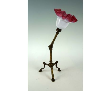 An Arts & Crafts brass adjustable desk lamp, raised on three Arts Nouveau feet, in manner of W A S Benson, with cranberry and