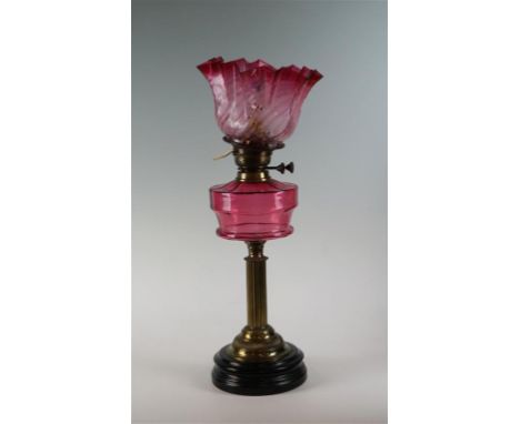 A late Victorian cranberry glass oil lamp, the stepped circular black stoneware base, adorned with  a brass Corinthian column