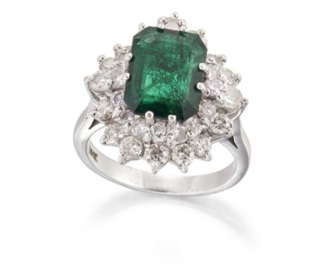 AN EMERALD AND DIAMOND CLUSTER RING, an octagonal-cut emerald in a double-claw setting and within an undulating two-tier bord