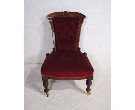 A Victorian red upholstered nursing chair, with button-back detailing and carved decoration, raised on turned legs