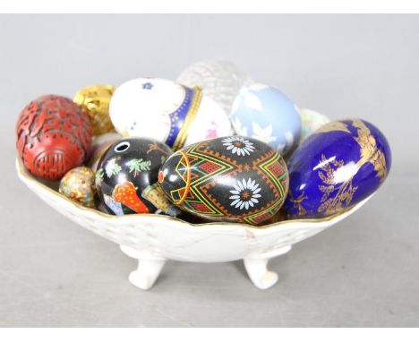 A bowl containing a collection of egg ornaments to include stone, glass, champlevé, cinnabar lacquer style, ceramic and simil