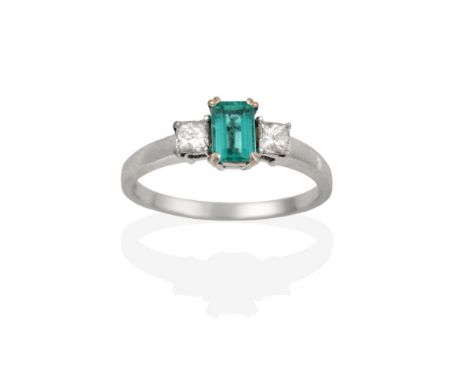 An 18 Carat White Gold Emerald and Diamond Three Stone Ring, the emerald-cut emerald flanked by princess cut diamonds, in cla