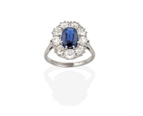 A Sapphire and Diamond Cluster Ring, the oval cut sapphire within a border of old cut diamonds, in white claw settings, to a 