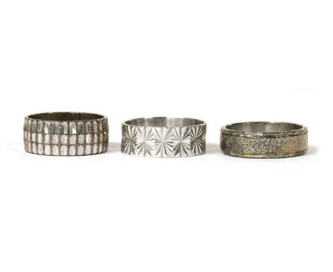 Three white gold wedding rings, to include an 18ct white gold star patterned flat section wedding ring, London, and two 9ct w