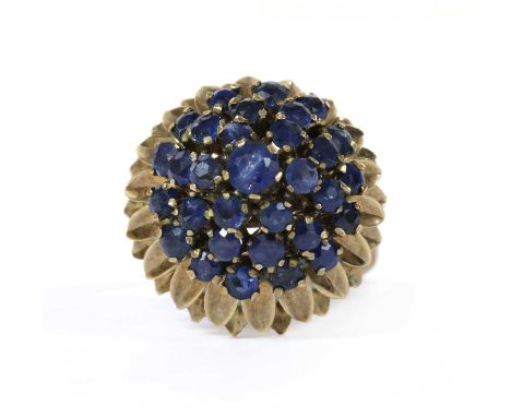 A gold sapphire cluster ring, with a central round mixed cut sapphire, claw set, to three round surround of round mixed cut s