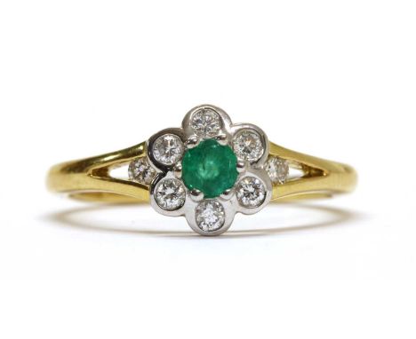 An 18ct gold emerald and diamond daisy cluster ring, with a round mixed cut emerald claw set at the centre, to surround of br