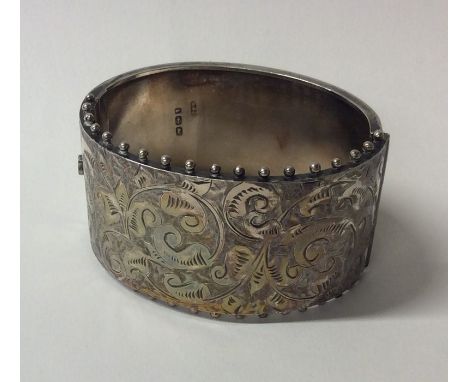 A Victorian silver hinged bangle with scroll decoration. Approx. 32 grams. Est. £30 - £40.