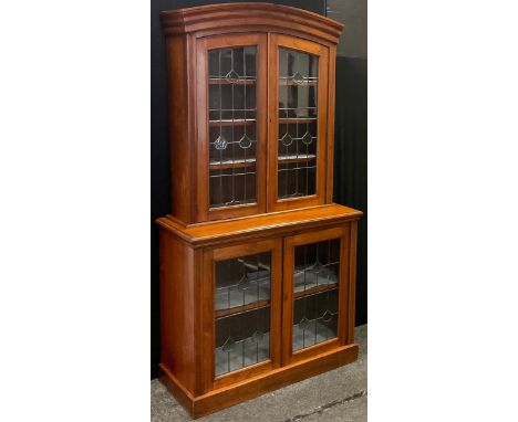 An Arts &amp; Crafts walnut display cabinet, arched pediment above two leaded stained and clear glass doors, deeper base, wit