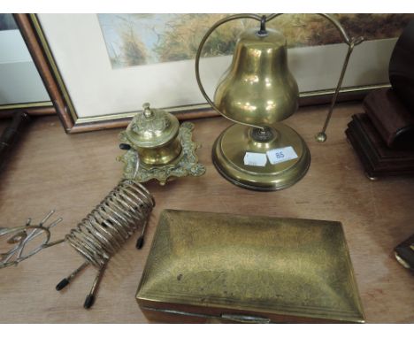 A selection of desktop items including a machined brass cigerette case, brass reception bell, and brass inkwell. 