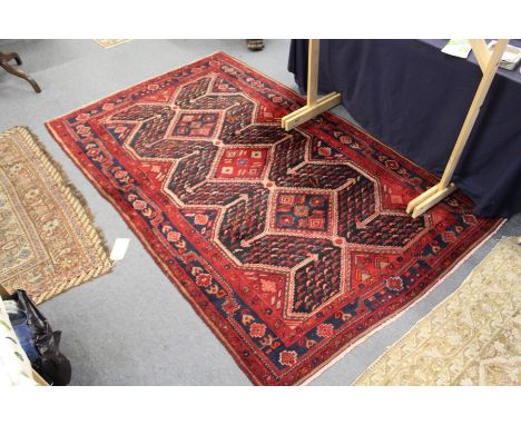 A Persian rug, red ground with three large diamond shaped central motifs.