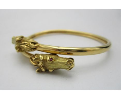 A Cartier style French gold double equestrian bangle, modelled with two horse heads inset with ruby eyes, stamped with lozeng