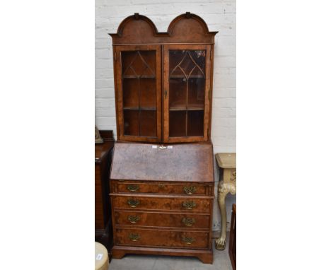 A reproduction burr yew wood bureau bookcase, the twin domed top above twin astregal glazed doors with fall fronted door with