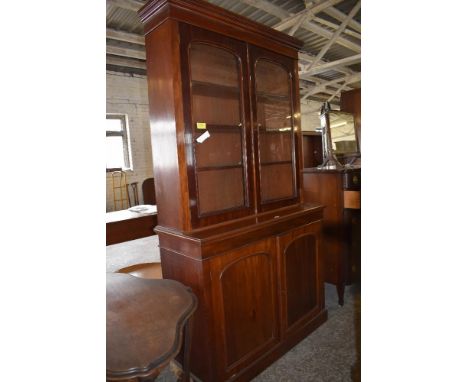 A Victorian mahogany bookcase over cupboard, having moulded cornice and plain frieze over two arched glazed doors enclosing a