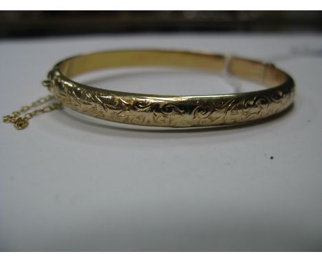 A 9ct Gold Bangle, leaf scroll engraved to the front, hinged to snap clasp.