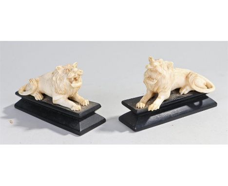 Pair of early 20th Century ivory lions, both in a reclining postion on black plinth bases, (2)