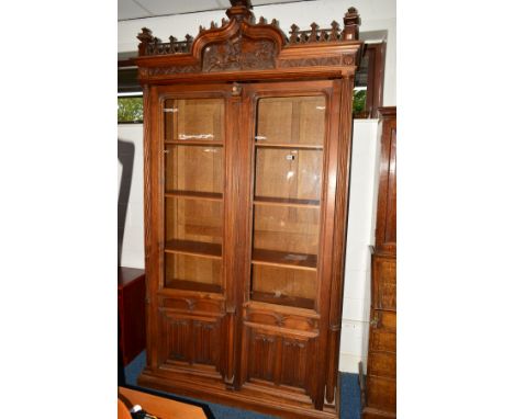 AN EARLY TO MID 20TH CENTURY OAK GLAZED DOUBLE DOOR BOOKCASE, the top with carved ecclesiastical decoration, central hunting 