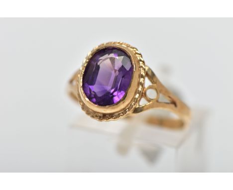 A 9CT GOLD AMETHYST SINGLE STONE RING, the oval cut amethyst collet set, within a rope twist surround, to the openwork should