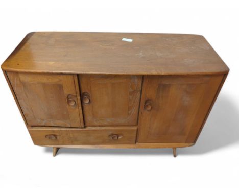 A mid-century Ercol Windsor elm sideboard, with twin-cupboard doors enclosing a shelf, flanked by a single cupboard, on taper