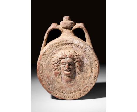Ca. 300 - 100 BC A mould-formed ornate terracotta flask of a Gorgon head with an elaborate hairstyle. The flask is surmounted