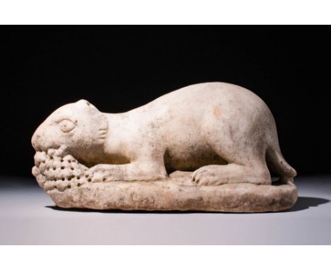Ca. AD 100 - 200 A Carved white marble hare crouching on an oblong, integral base and gnawing a clump of grapes or barries, w