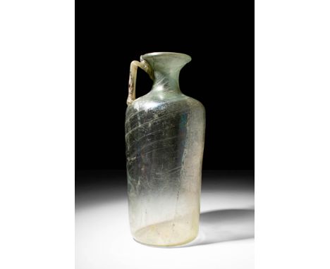Ca. AD 100 - 300 A Roman pale green glass mould-formed bottle. The vessel is defined by a slightly concave base and a cylindr