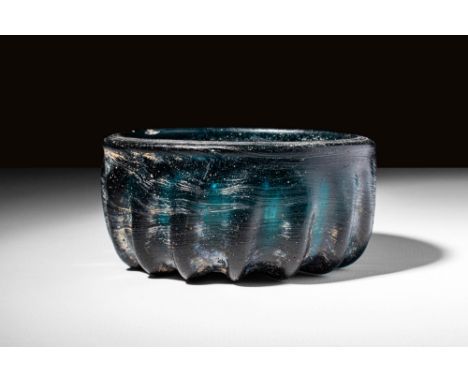 Ca. 100 BC - AD 100 A thickly-ribbed bowl in dark blue glass. It is mould-made, cast in a shallow phiale-like form, with a sl