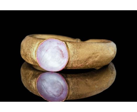 Ca. AD 300 A Roman gold ring with a simple and elegant round hoop that secures a pink quartz stone depicting magical symbols.