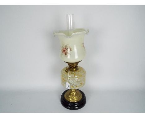 An oil lamp with black ceramic base and brass support below a mottled glass reservoir and floral decorated shade, approximate