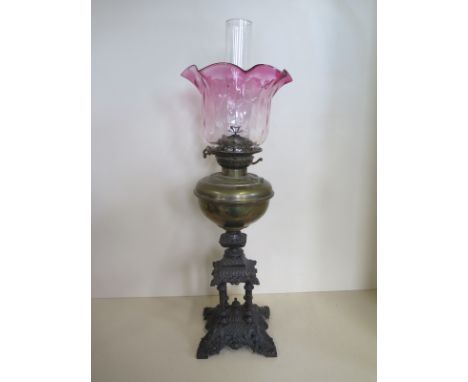 An oil lamp with cast iron base, brass font and cranberry tinted shade, 69cm tall including chimney 