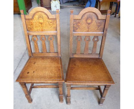 A pair of early 20th Century oak Hall Chairs of Liberty style, the panel backs inlaid with stylised peacock feathers above pa