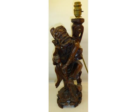 An oriental carved wood Figure holding a stick, 17" (43cms) high, used as a table lamp.