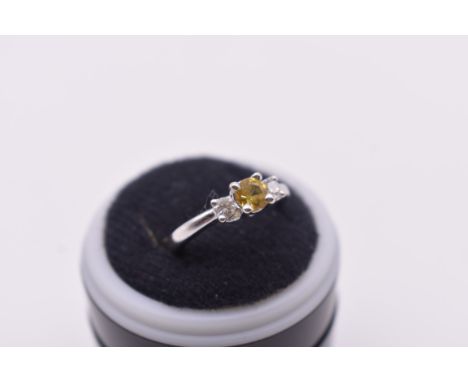 An 18ct white gold diamond three stone ring, set central yellow brilliant cut diamond with a brilliant cut diamond to each si