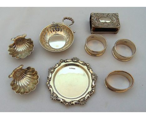 A quantity of hallmarked silver to include two shell shaped salts, three napkin rings, a coaster, a wine taster and a matchbo