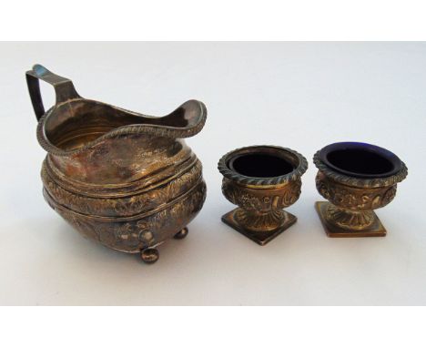 A Georgian hallmarked silver cream jug with angled handle on four ball feet and a pair of urn shaped hallmarked silver salts 