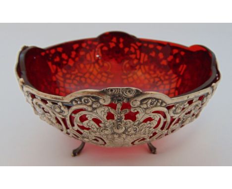 A continental white metal pierced circular dish with red glass liner on four scroll legs, 8.5 x 16cm