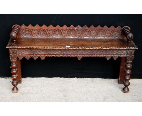 Oak hall bench, the raised carved back panel flanked by ring turned arms, rectangular seat, matching apron, raised on ring tu