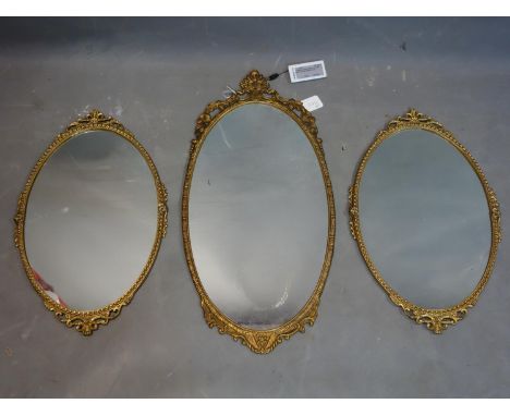 A pair of gilt metal oval mirrors, with scrolling floral finial, H.53 W.35cm, together with a gilt oval mirror with pierced f