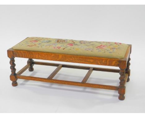 An early 20thC oak duet stool, with a floral wool work tapestry seat, raised on spiral twist columns, united with by a box st