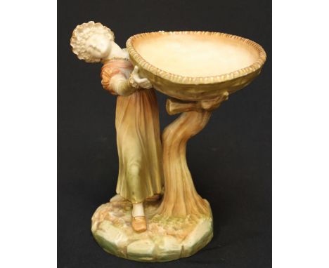 A 1903 blush ivory Royal Worcester figural comport, with a girl wearing a bonnet, holding aloft a large oval bowl supported b