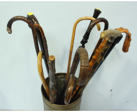 An embossed brass walking stick stand, together with a quantity of assorted walking sticks, most with curved handles.