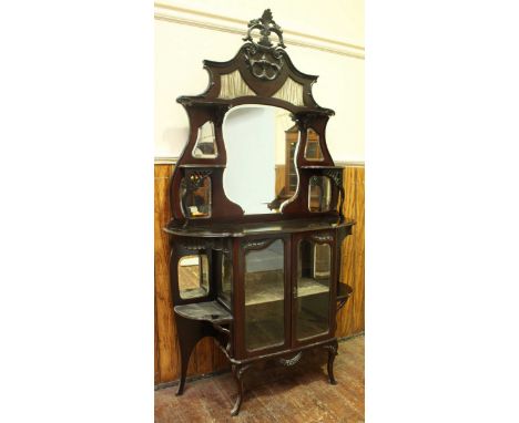 A carved Edwardian mahogany cabinet with floral finial, shaped central mirror and ornament shelves above two glazed doors and