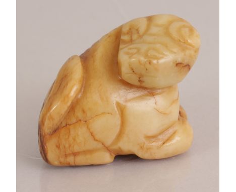 A CHINESE YELLOW JADE CARVING OF A BUDDHISTIC LION, its head turned backwards, the stone with russet inclusions, 1.9in long &