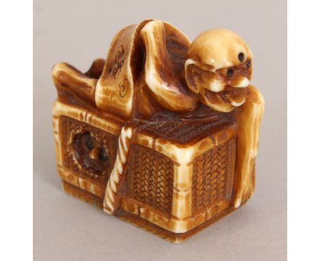 A SIGNED JAPANESE MEIJI PERIOD STAINED IVORY NETSUKE OF A DEMON, wrapped in a scroll and lying on top of a woven box from the