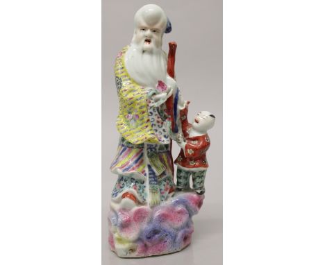 AN EARLY 20TH CENTURY CHINESE FAMILLE ROSE PORCELAIN FIGURE OF SHOU LAO, standing on rockwork in the company of a boy and bea