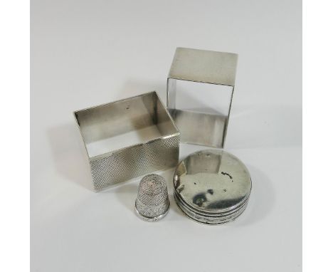 A pair of silver rectangular napkin rings with engine turned decoration, a size 14 silver thimble and a silver lid fitting wi