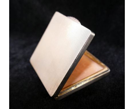 A square silver powder compact, with engine turned decoration, rose coloured thumb piece, and gilt interior, the lid set with